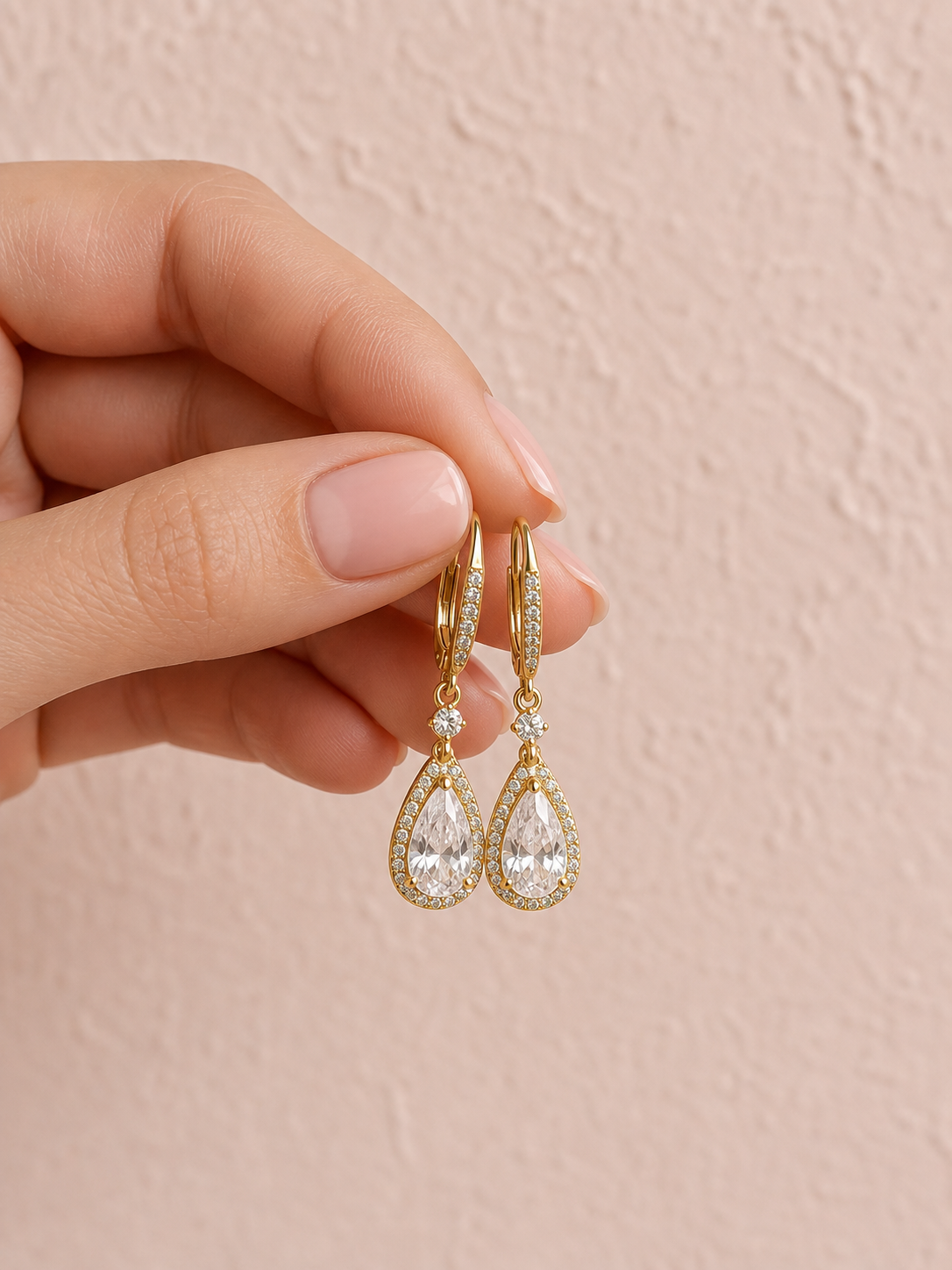 A woman's hand with neat manicured nails gently holding a pair of elegant gold drop earrings